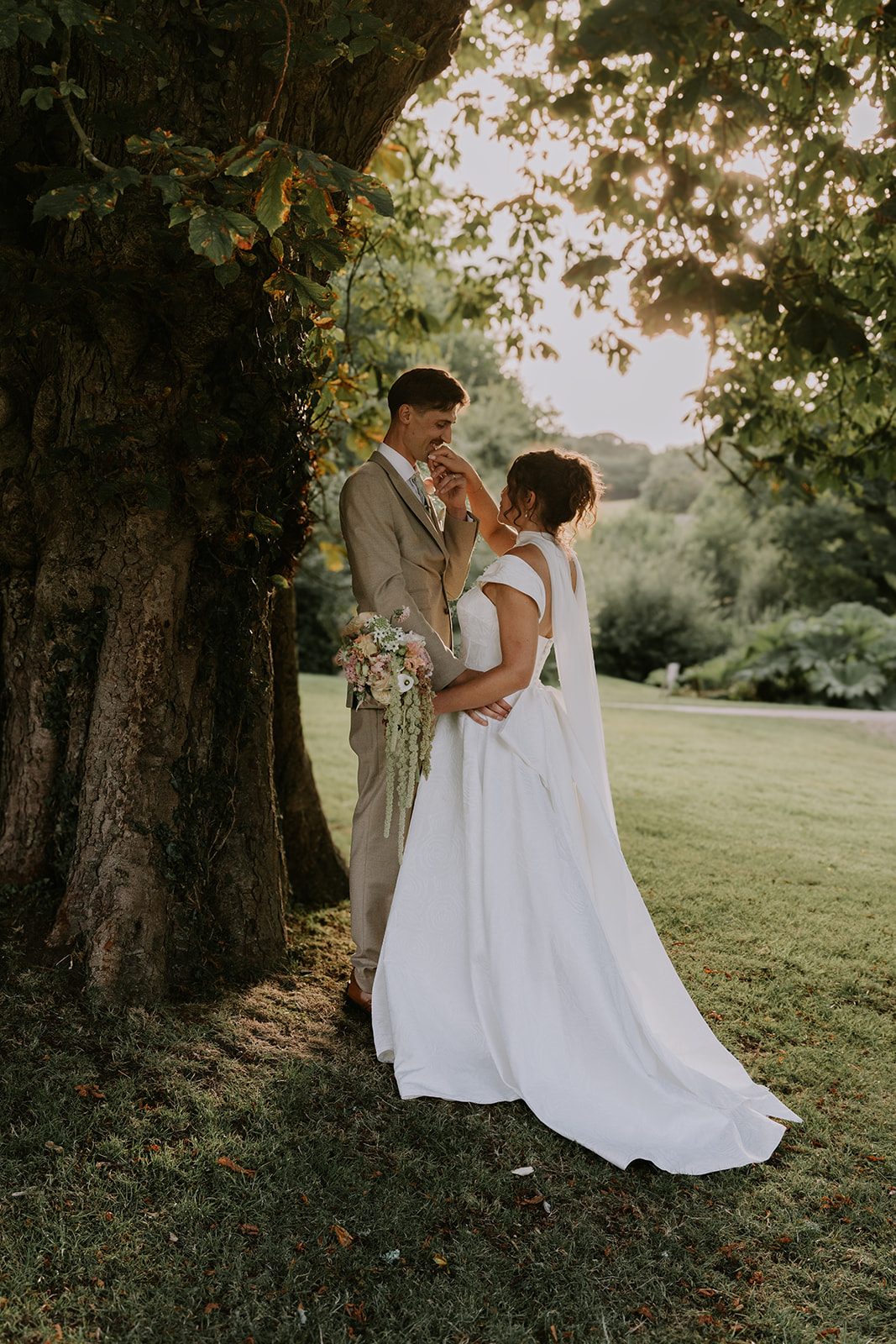 Amelia and Osh sharing a tender moment beneath a sunlit tree at Colehayes Park