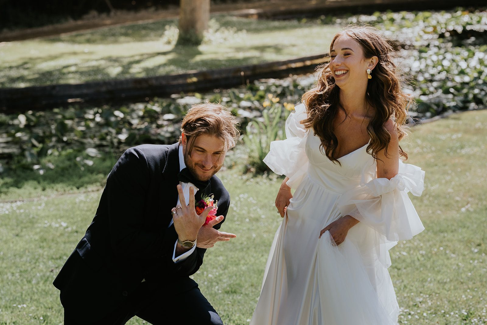 Ben and Leah laughing and showing their wedding rings beside the pond