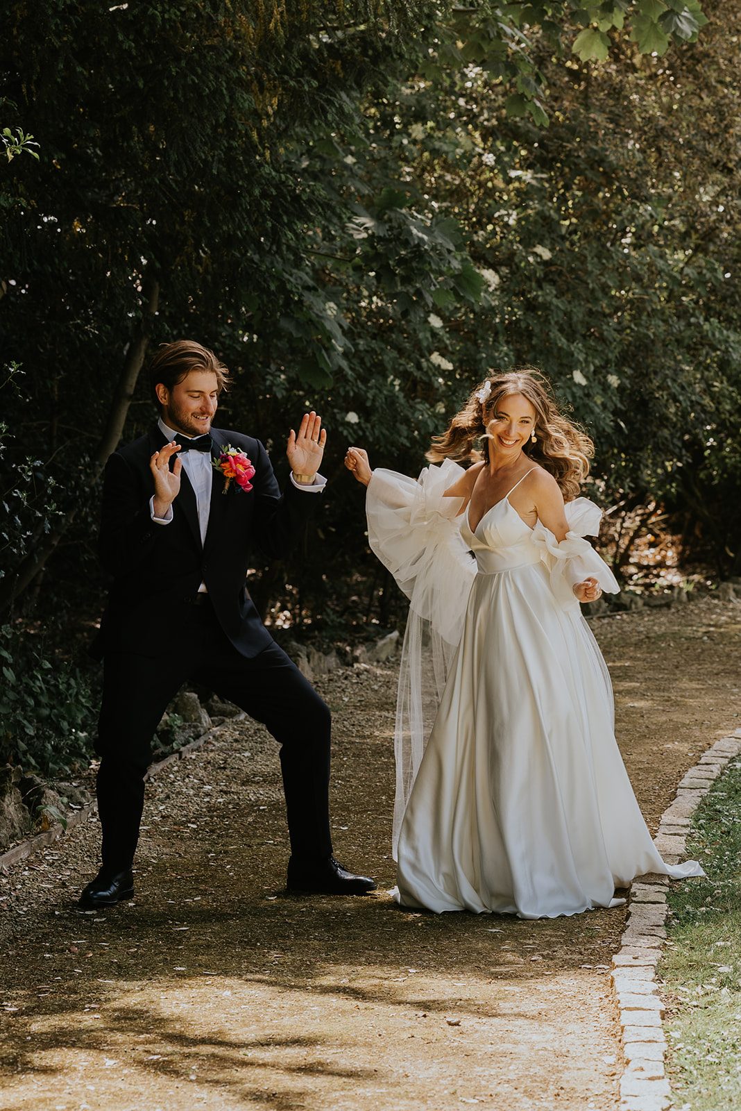 Ben and Leah laughing and dancing together on a garden path