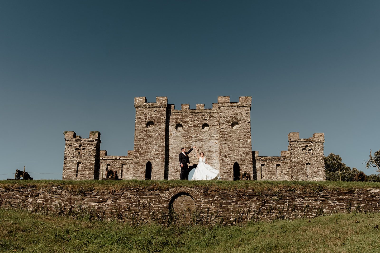 Charlotte and Nathan dancing in front of a stone castle beneath a blue sky
