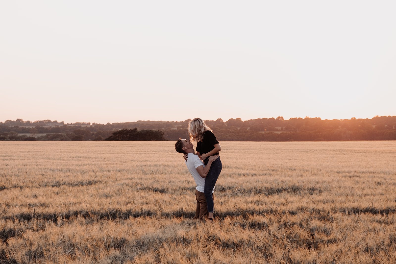 Kelly and Matt sharing a kiss in a golden field at sunset