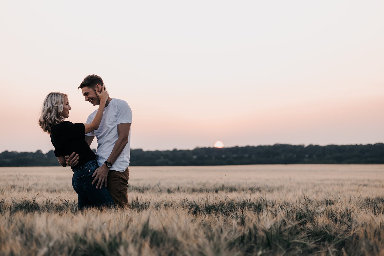 Kelly and Matt smiling together in a wheat field as the sun sets