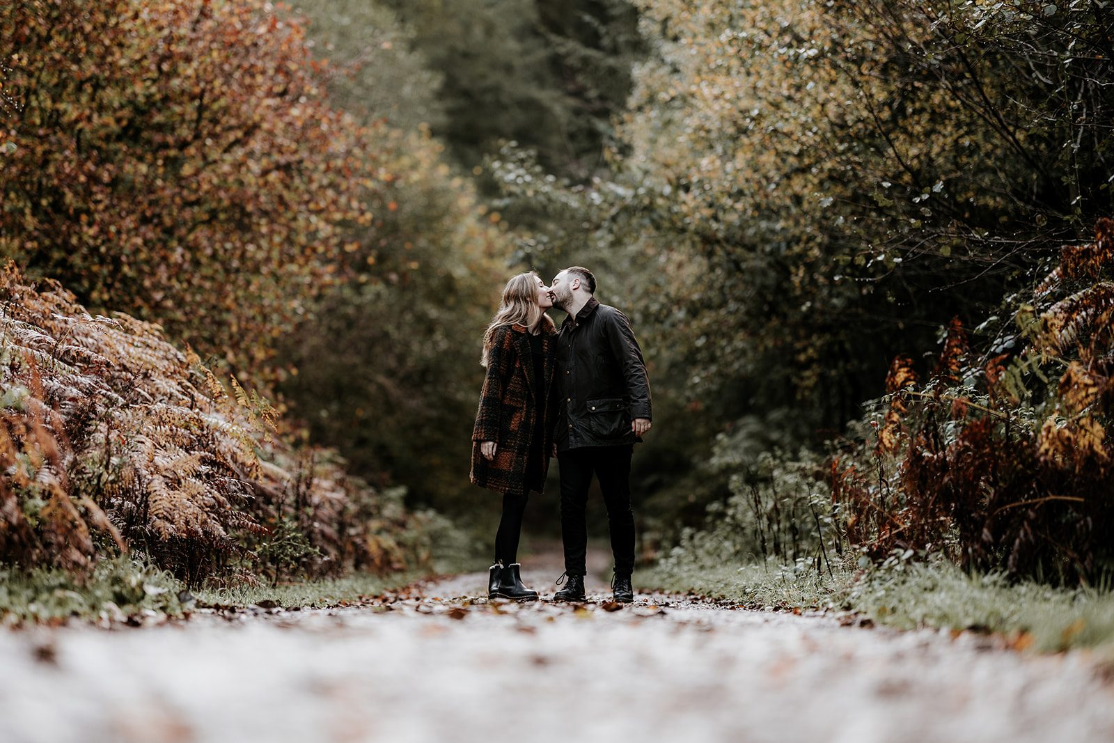 Laura and Sam kissing on an autumn woodland path