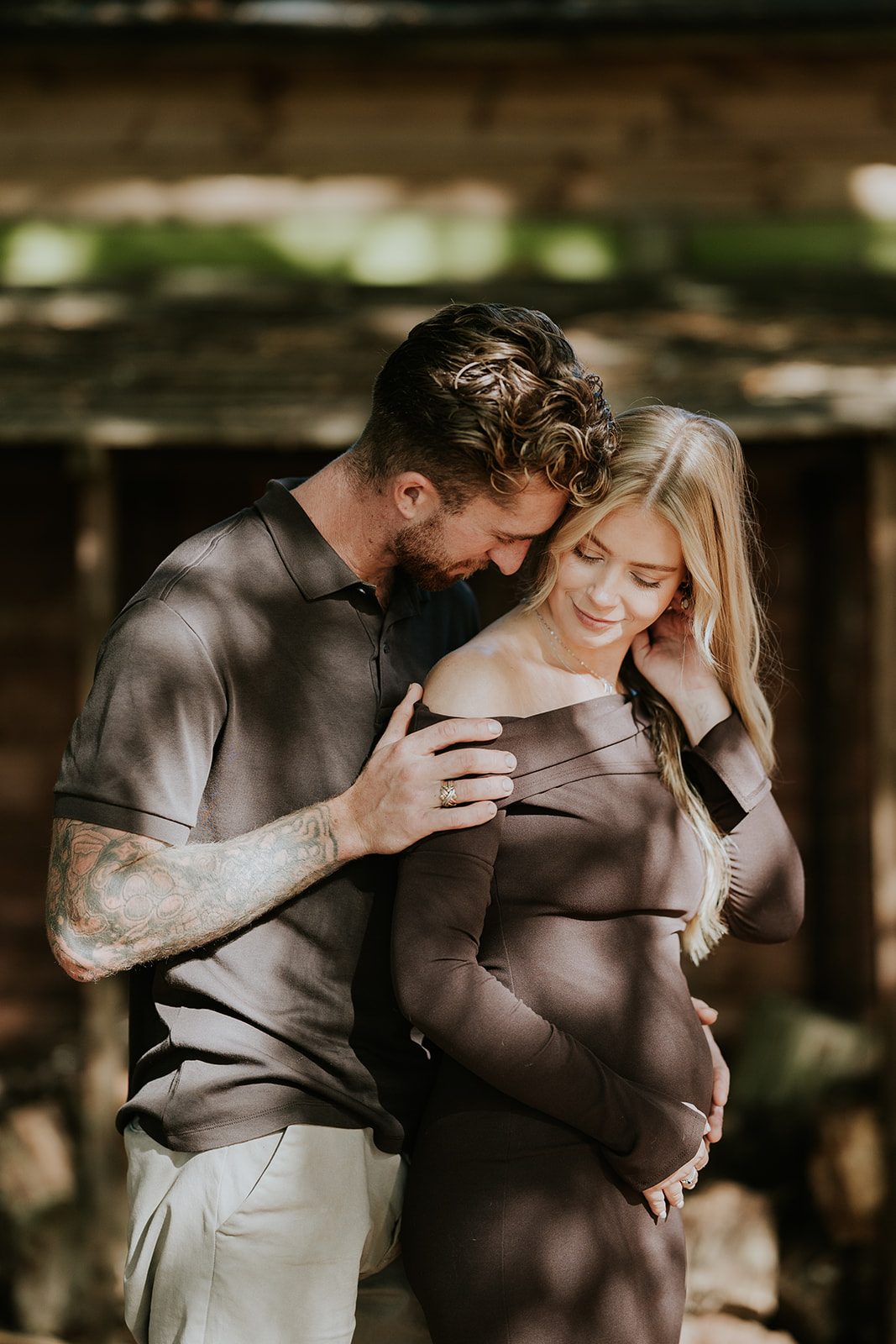 A couple holding the baby bump in dappled woodland light