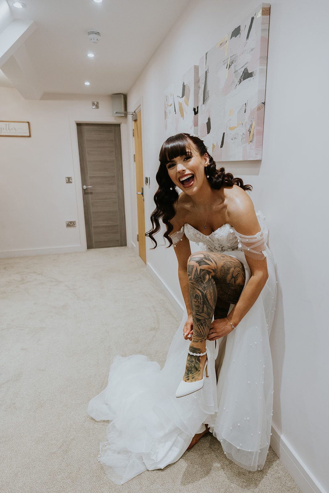 Danielle laughing as she fastens her wedding shoe, with her tattooed leg raised