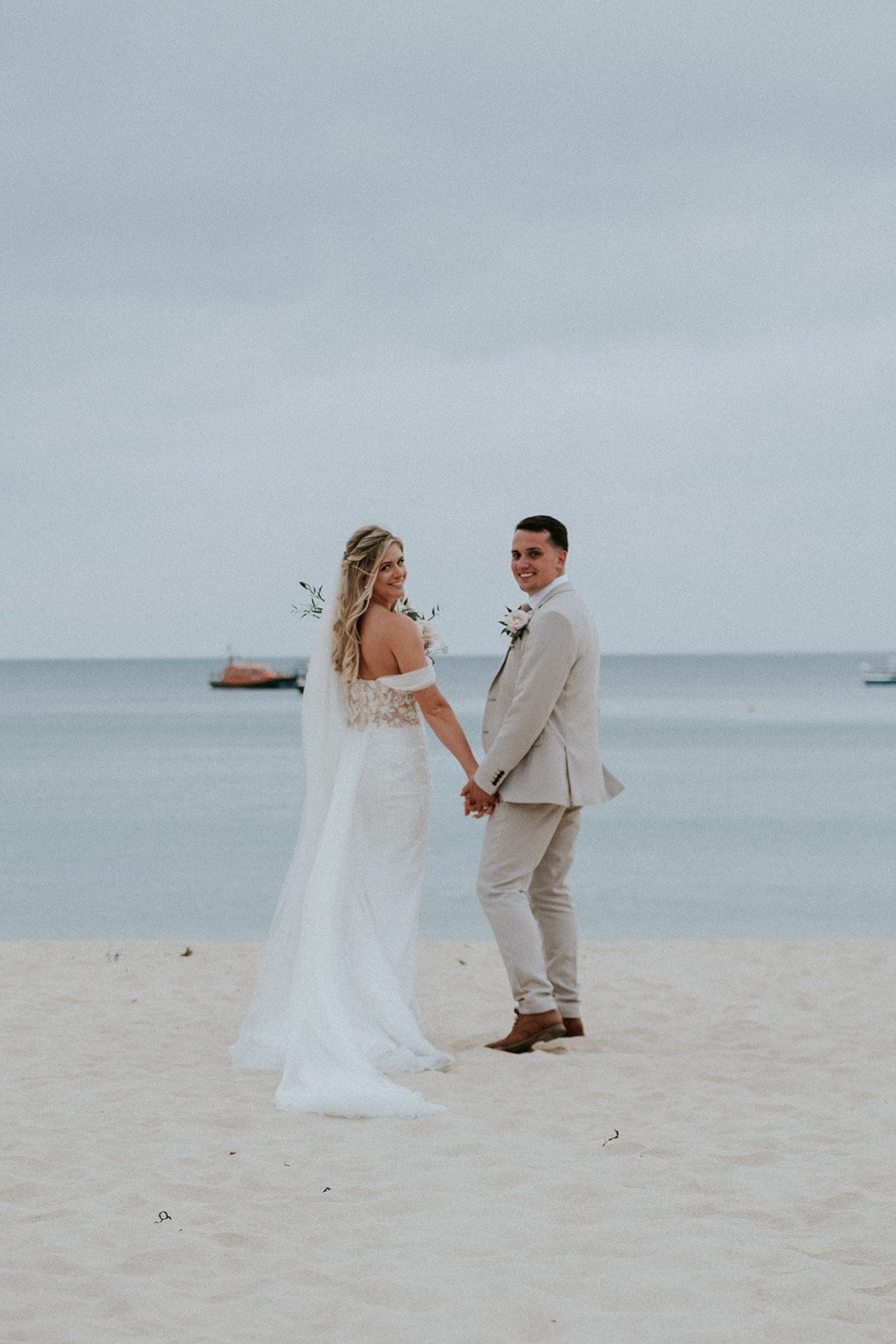 Hannah and Sonny holding hands and looking back on the beach