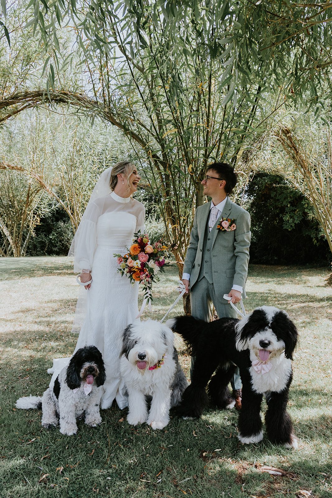 India and Cam laughing together beneath a willow with their three dogs