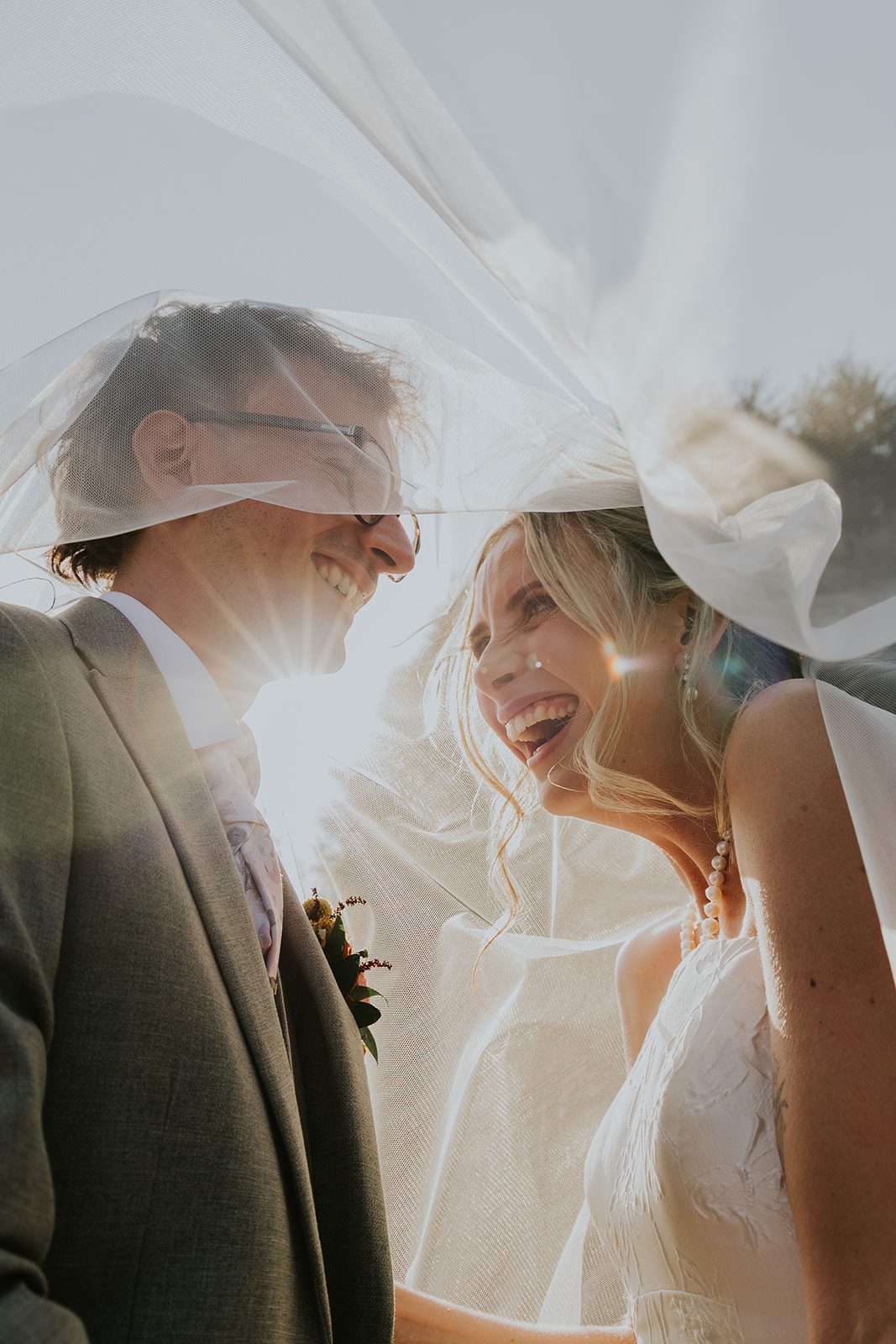 India and Cam laughing beneath the veil in warm sunlight