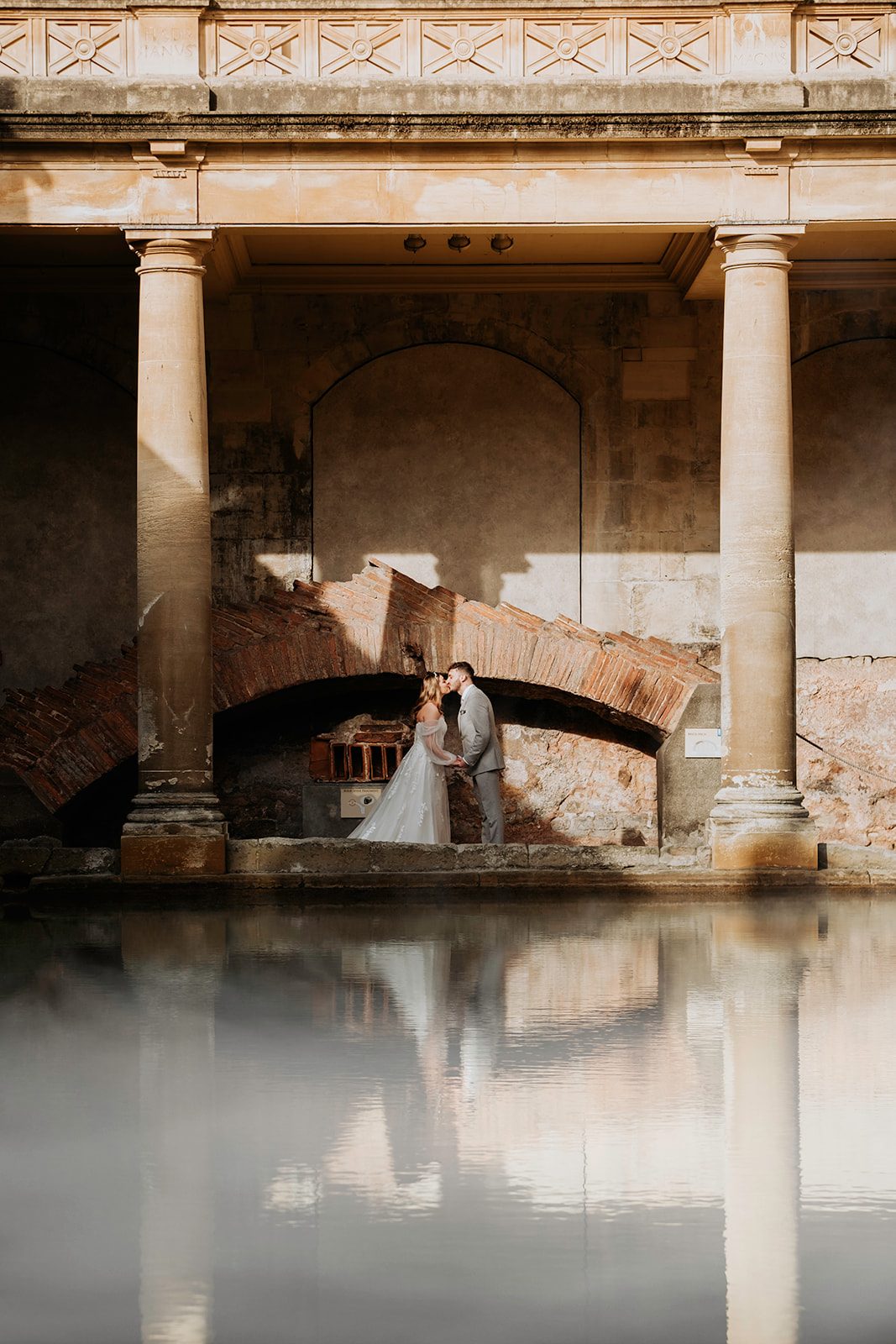 Isabelle and Dean reflected across the steaming water at the Roman Baths