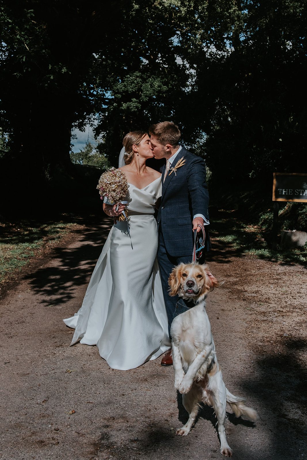 Megan and Sam kissing with their dog standing beside them