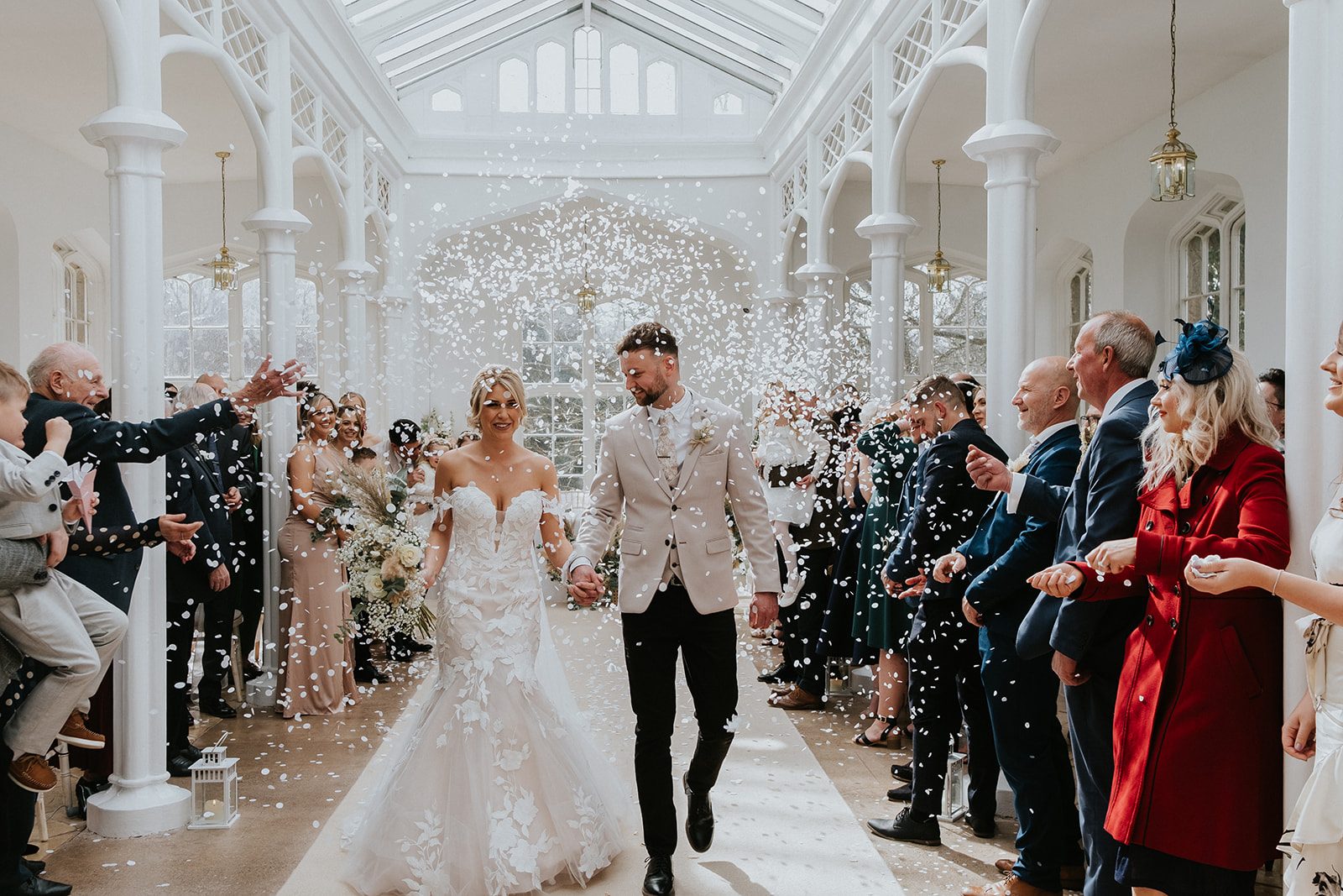 Si and Bryonny walking through confetti inside the St Audries orangery