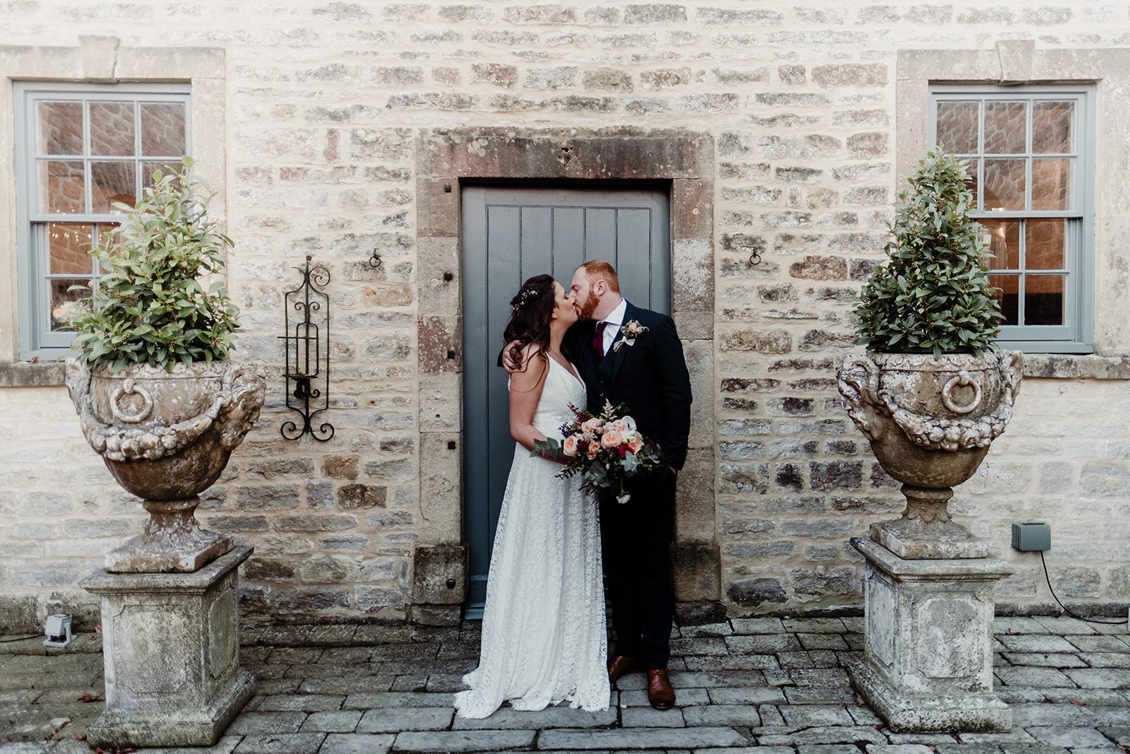 Yaz and Jack kissing in a stone doorway between two planted urns