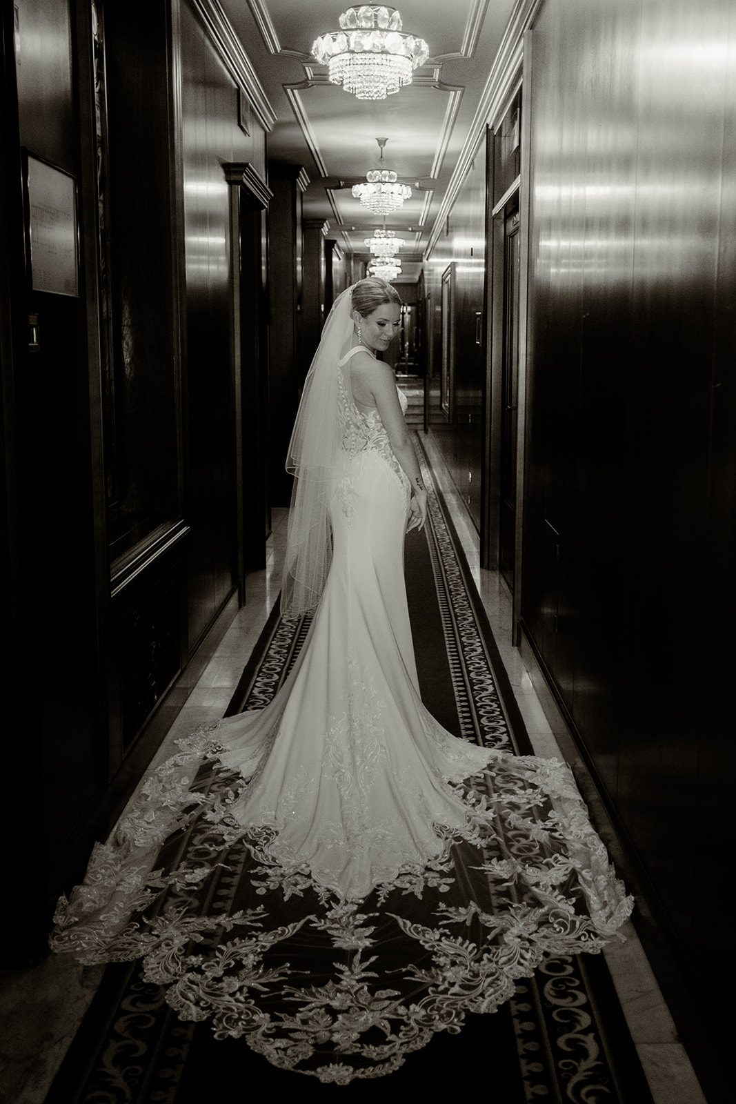 Zoe looking over her shoulder with her wedding dress train in a chandelier-lined hallway at Lake Bled